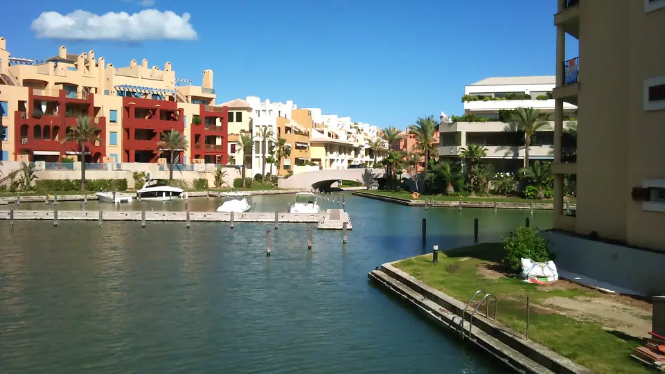 Apartment buildings and palm trees around a canal of the marina at Puerto Sotogrande