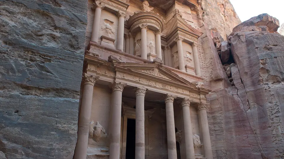 The carved rose-coloured facade of the Treasury, Al-Khazneh, between the sandstone cliffs of Petra