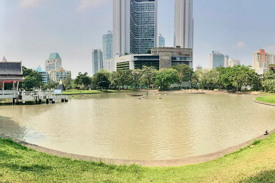 The lake and lawns of Benchasiri Park with high-rise buildings rising behind the trees