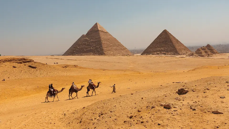 A camel caravan crossing the desert sand in front of the Giza pyramids of Khafre and Khufu