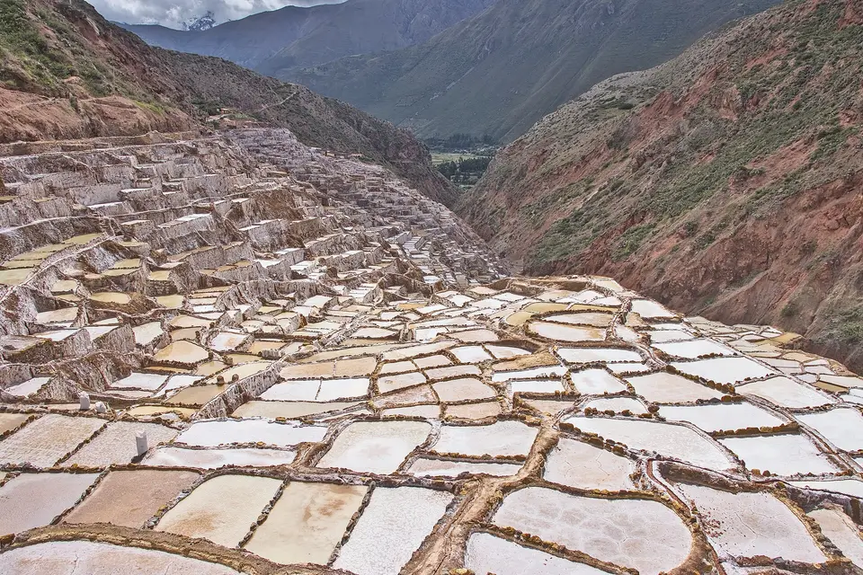 Hundreds of white salt pans stepping down a red hillside at the Maras salt mines