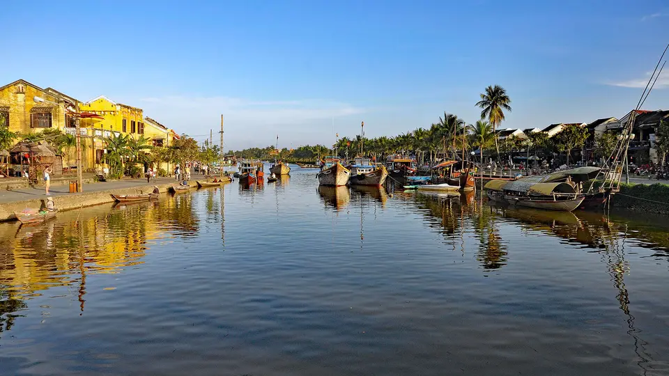 Old yellow shophouses along the Thu Bon River in Hoi An, reflected in the water in late sun