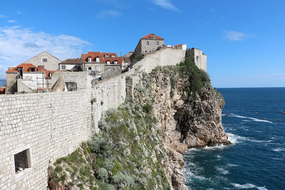 The stone city walls of Dubrovnik running along a rocky cliff above the blue Adriatic Sea