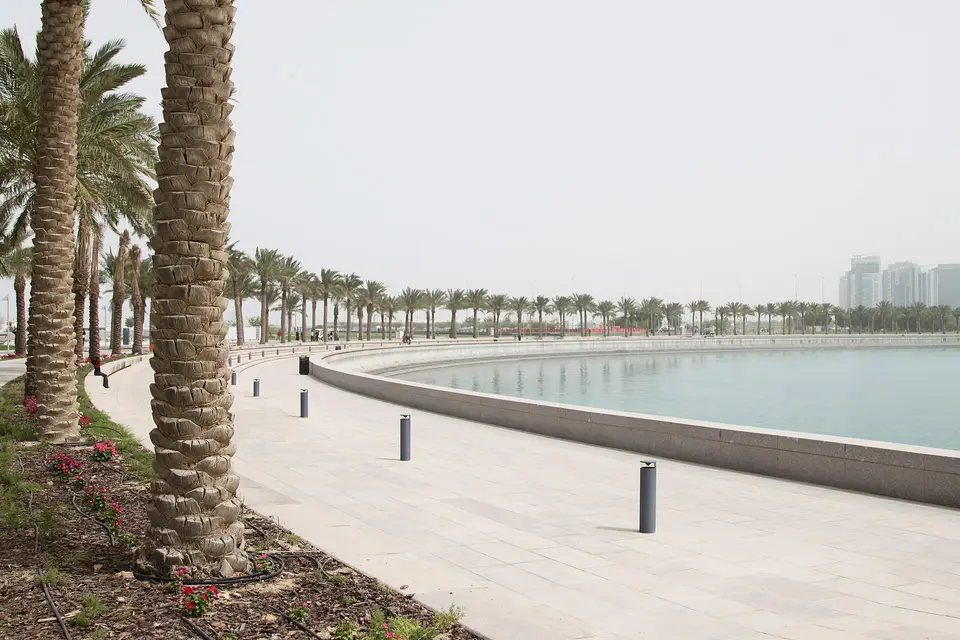 A palm-lined promenade curving along the water on the Doha Corniche