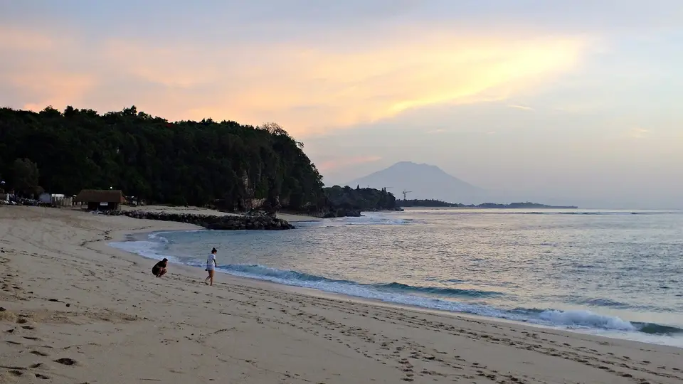 Nusa Dua beach at sunrise, with a wooded headland and a distant volcano on the horizon