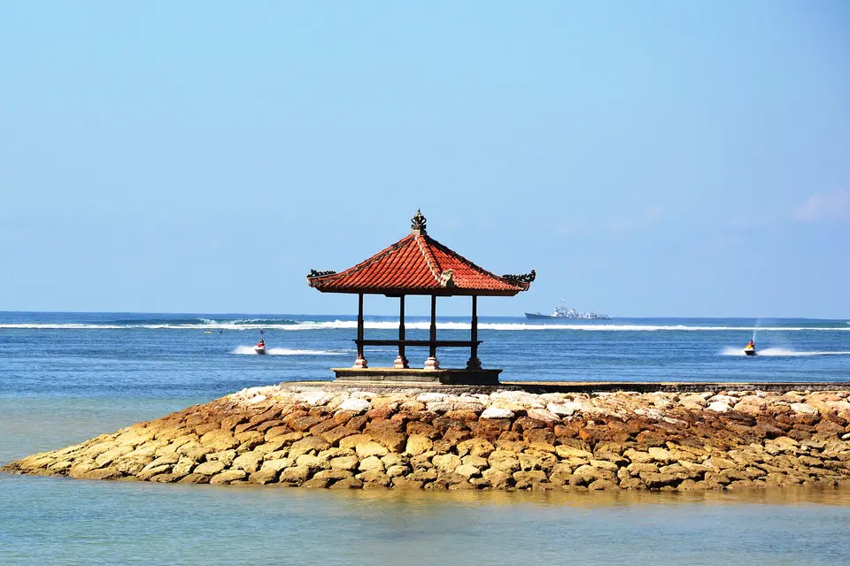 A red-roofed Balinese pavilion on a stone breakwater at Tanjung Benoa, beside Nusa Dua