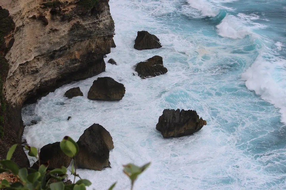 Waves breaking around dark rocks at the foot of the Uluwatu cliffs, Bali