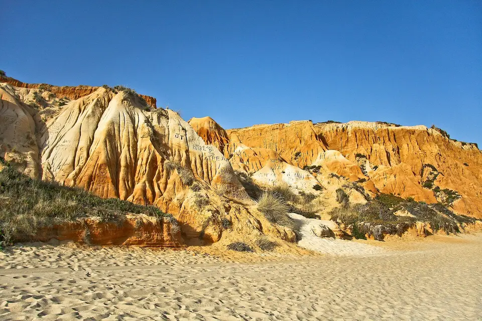 Red and ochre sandstone cliffs above the sand at Praia da Falésia under a clear blue sky