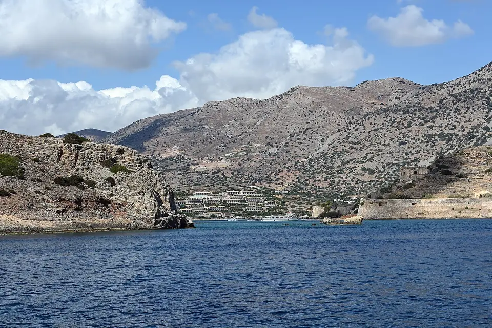 The rocky shore of Spinalonga and the village of Plaka below bare mountains across the strait