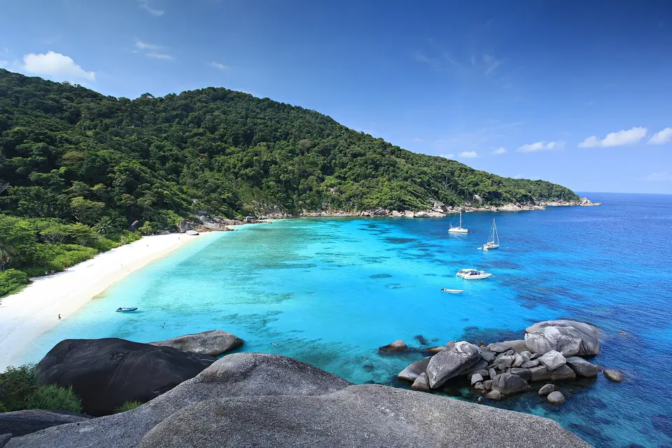 Turquoise water and a white sand beach below forested hills in the Similan Islands
