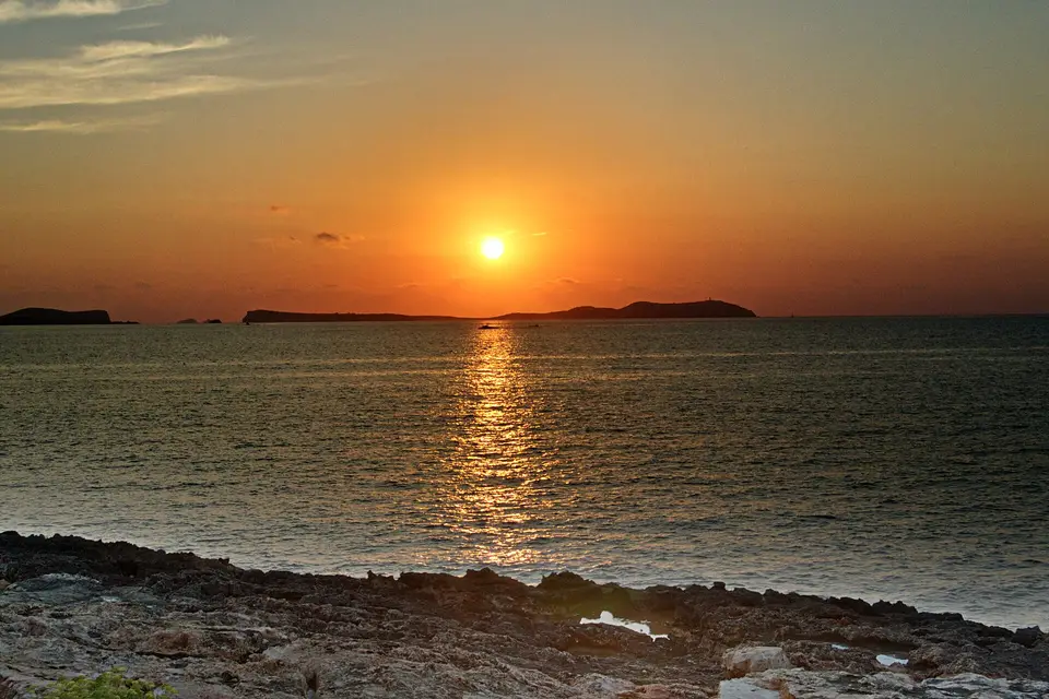The sun setting over the sea and offshore islets from the rocky shore of San Antonio