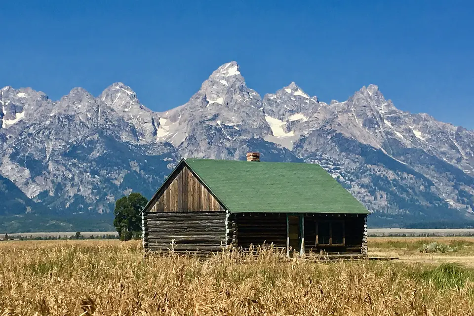 A weathered log barn on Mormon Row below the jagged peaks of the Grand Teton