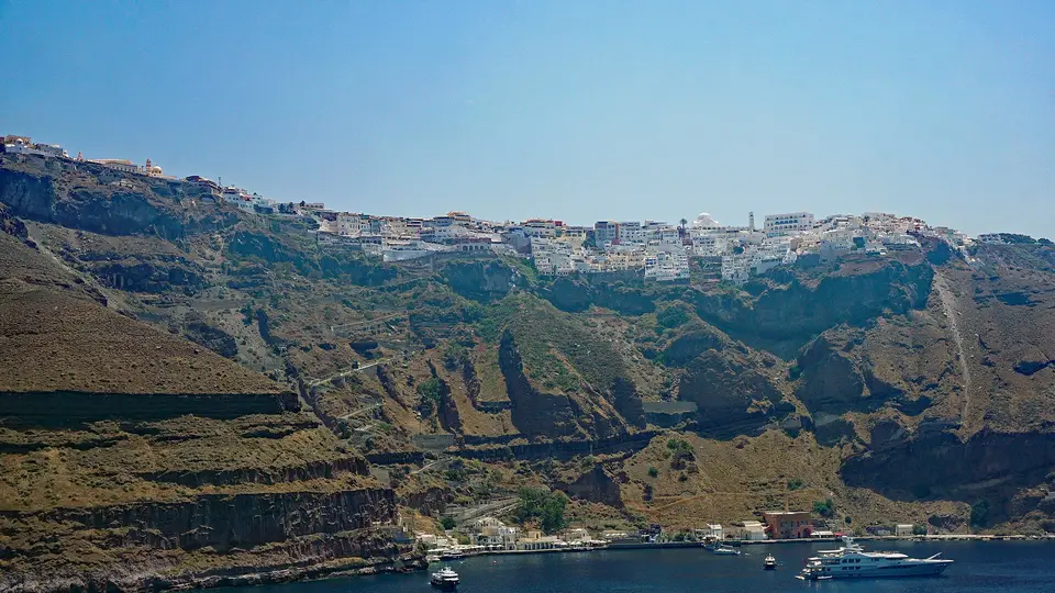 The white houses of Fira lining the caldera cliff top above the old port, seen from the sea