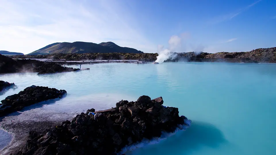 Milky blue water of the Blue Lagoon between black lava rocks, with geothermal steam rising