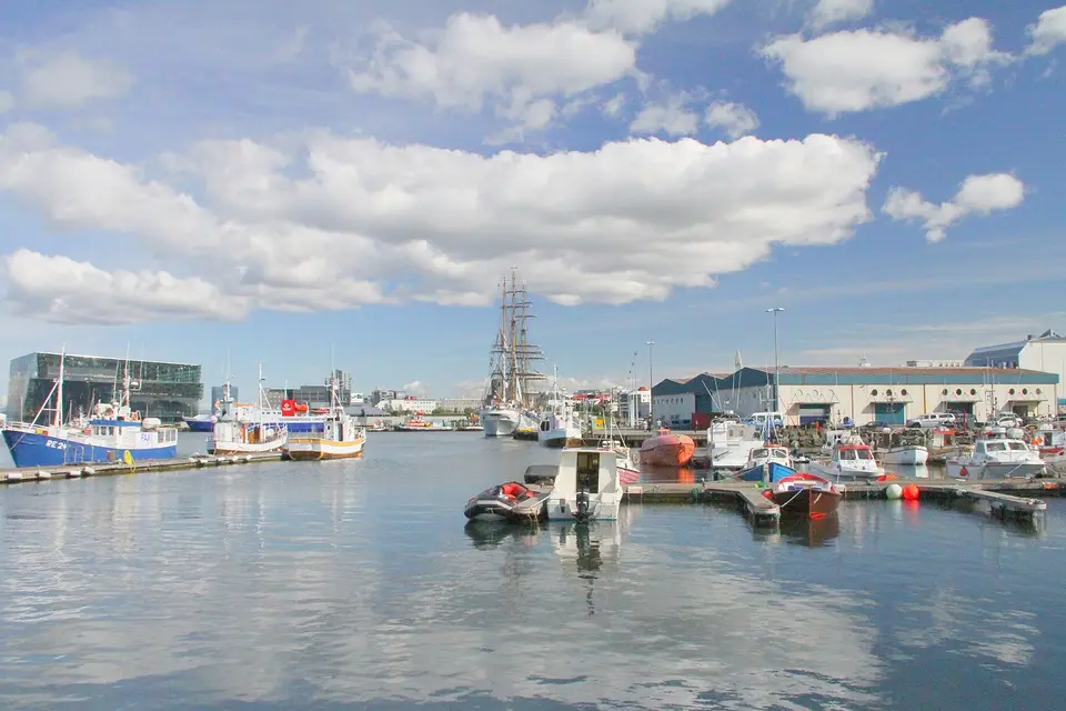 Fishing boats and a tall ship moored in the Old Harbour of Reykjavík, with Harpa on the left