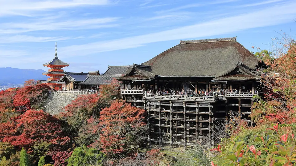 Kiyomizu-dera in Kyoto, its wooden hall and pagoda rising above red autumn maples on the hillside