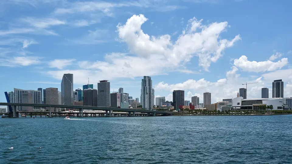 The downtown Miami skyline and a causeway bridge across Biscayne Bay under scattered white clouds