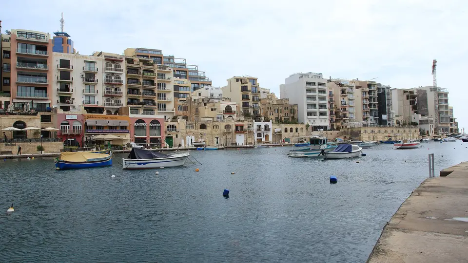 Small boats moored in the calm water of Spinola Bay, lined by the apartments of St Julian's
