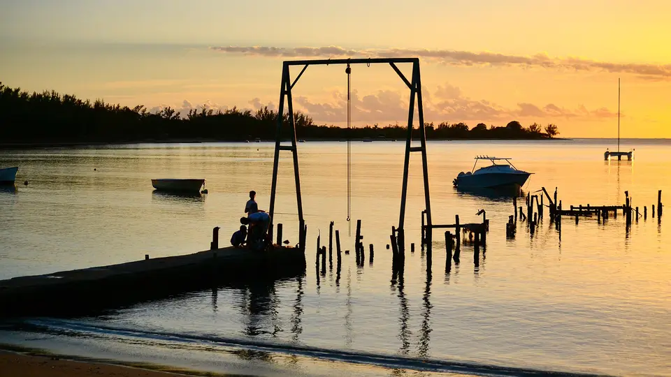 Sunset over the calm lagoon at Belle Mare, with a small jetty, old wooden posts and boats at anchor