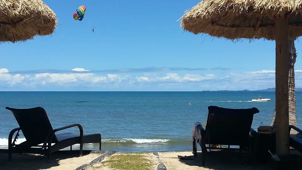 Sun loungers under thatched umbrellas facing the blue sea on the beach at Denarau Island