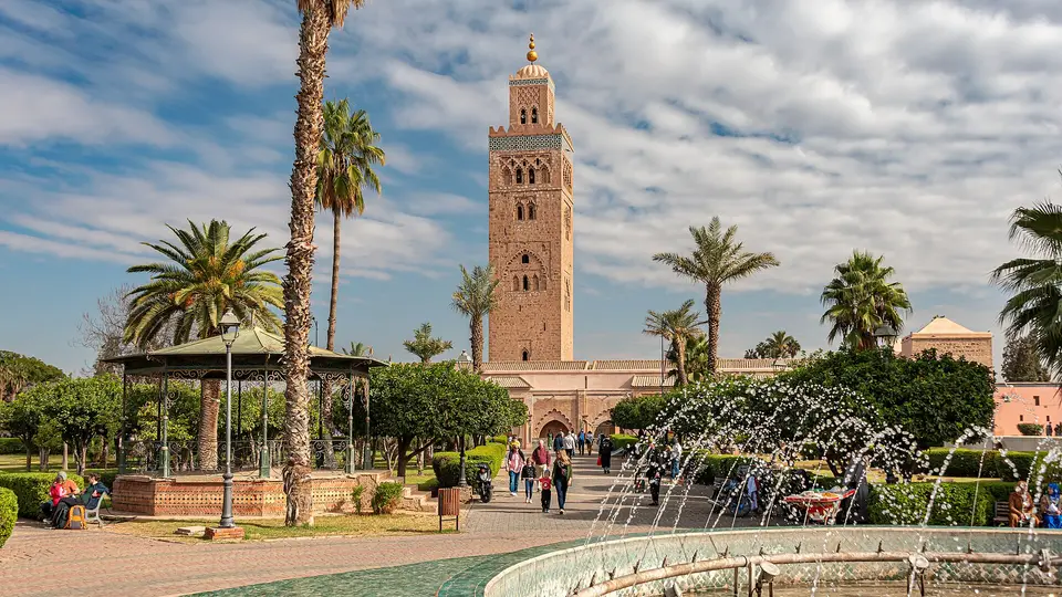 The Koutoubia minaret in Marrakech rising above palm trees and gardens under a cloudy sky