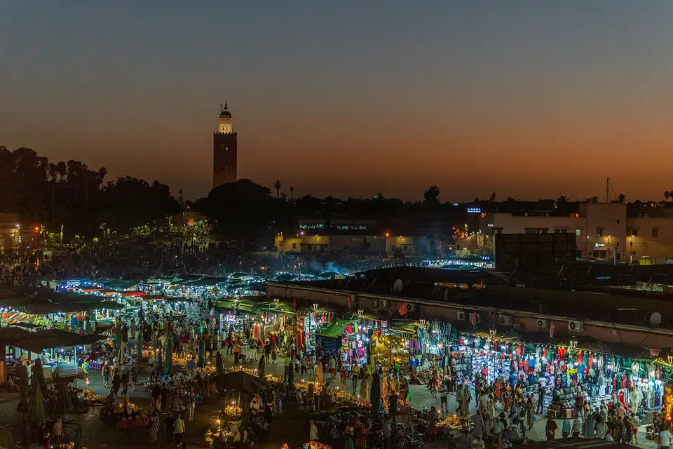 Jemaa el-Fnaa square glowing with food stalls at dusk, with the Koutoubia minaret in the distance
