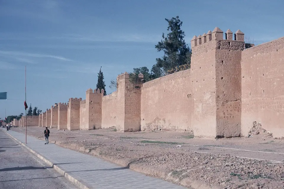 Long red-earth ramparts with square towers beside a road outside the medina