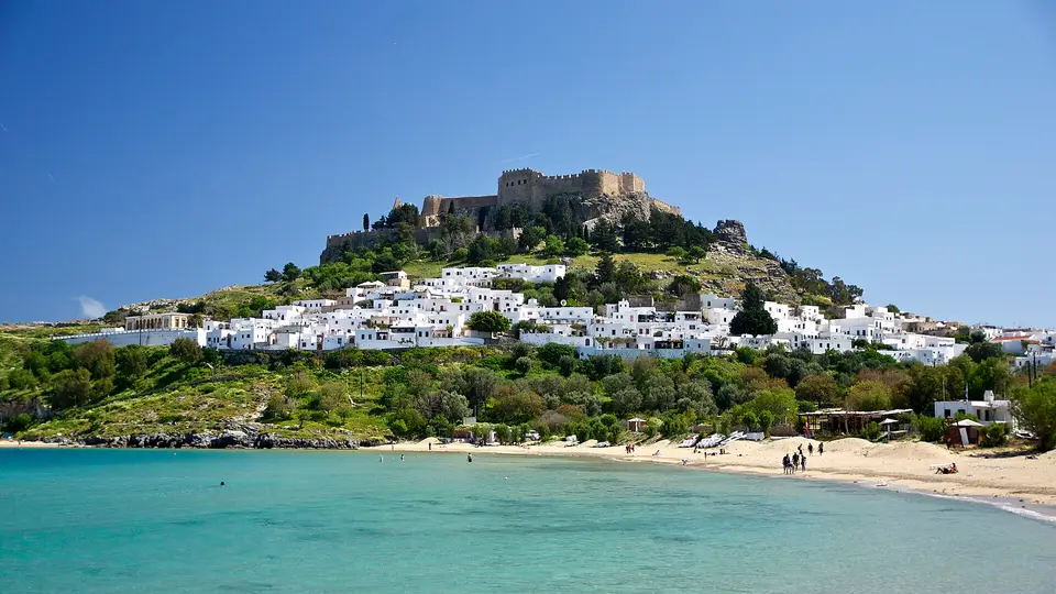 White houses of Lindos village climbing the hill below the acropolis, above the turquoise bay