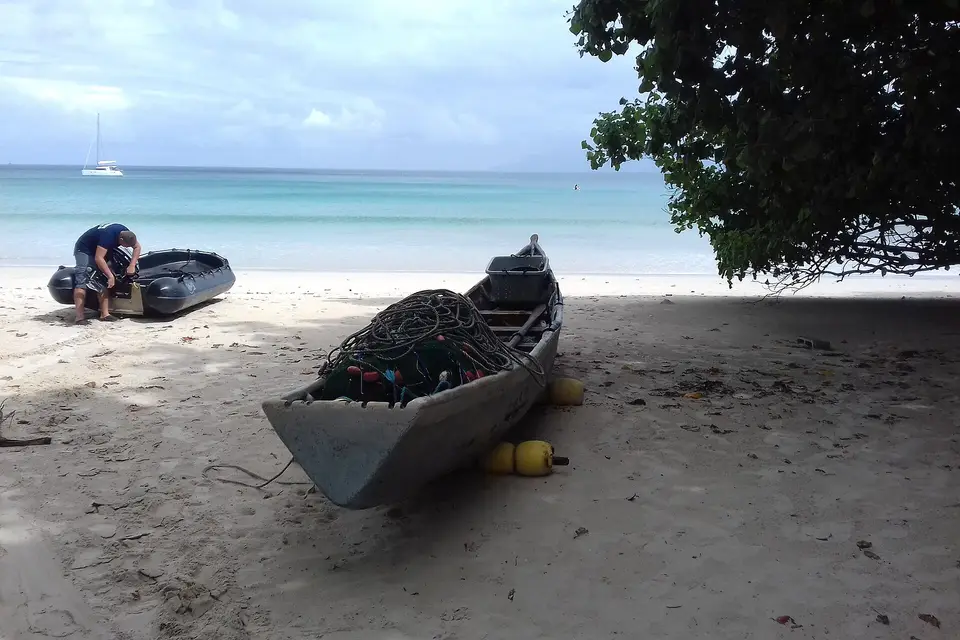 A wooden fishing boat pulled up on the sand of Beau Vallon beach under a shady tree