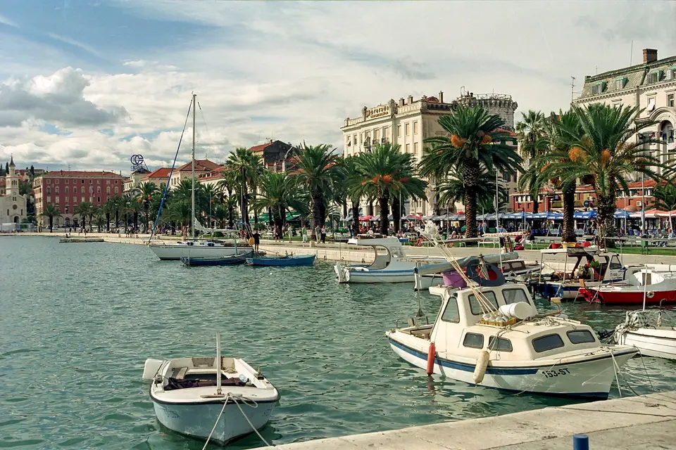 Small boats moored beside the Riva promenade, lined with palm trees and old facades