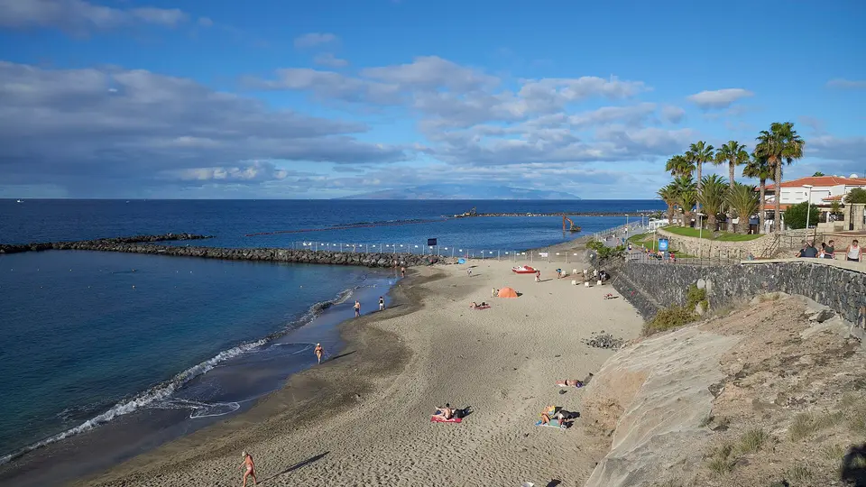 The sandy curve of Playa del Duque in Costa Adeje, with palms and a calm sea under blue sky