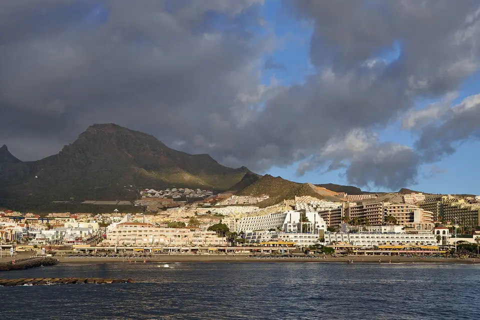 Hotels along the Costa Adeje seafront below a volcanic peak, seen from the sea under heavy clouds
