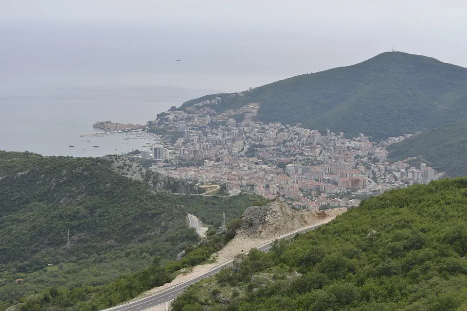 Budva and its old town peninsula seen from the wooded hills, with a road winding below