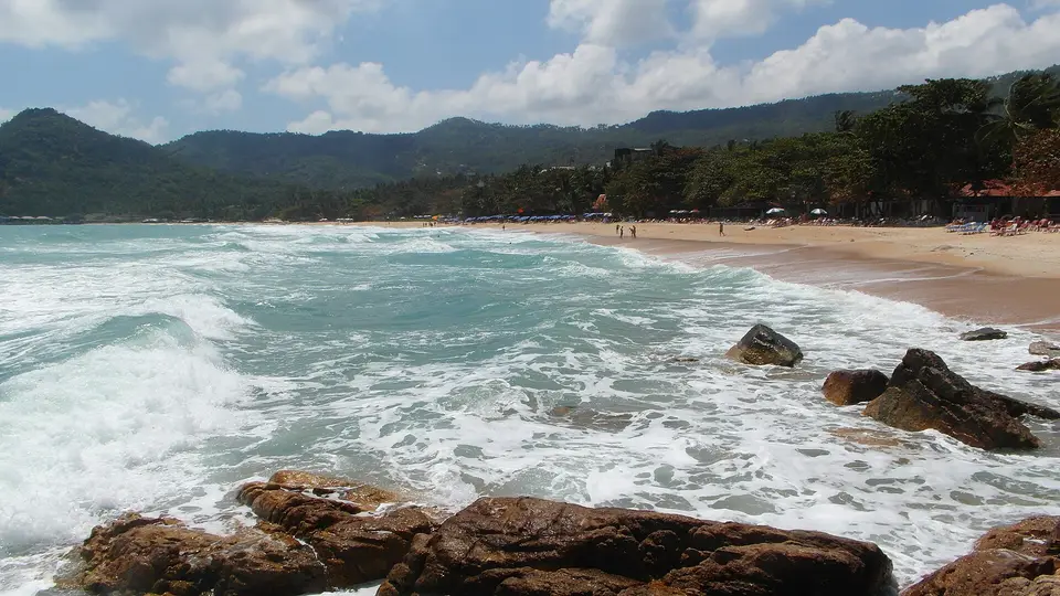 Waves rolling onto the curving sand of Chaweng Noi beach below forested hills on Koh Samui