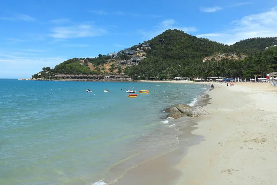 Calm turquoise water and white sand at Chaweng Noi beach, Koh Samui, with green hills behind