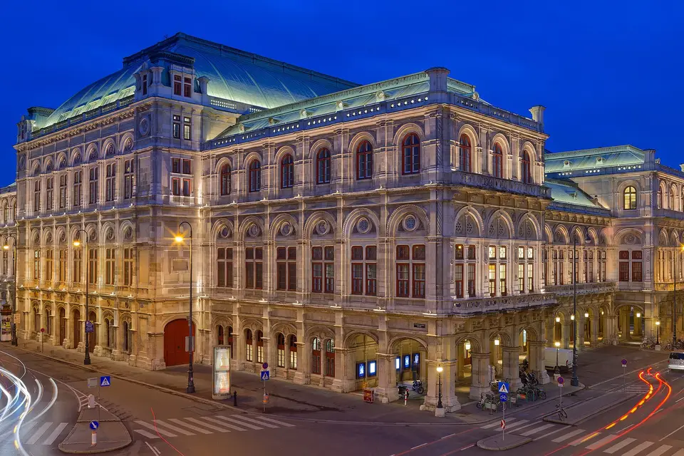 The Vienna State Opera on the Ringstrasse at blue hour, its facade lit against a deep blue sky